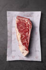 Raw NY strip steak with marbling and fat cap on Campo Grande branded paper wrapping.