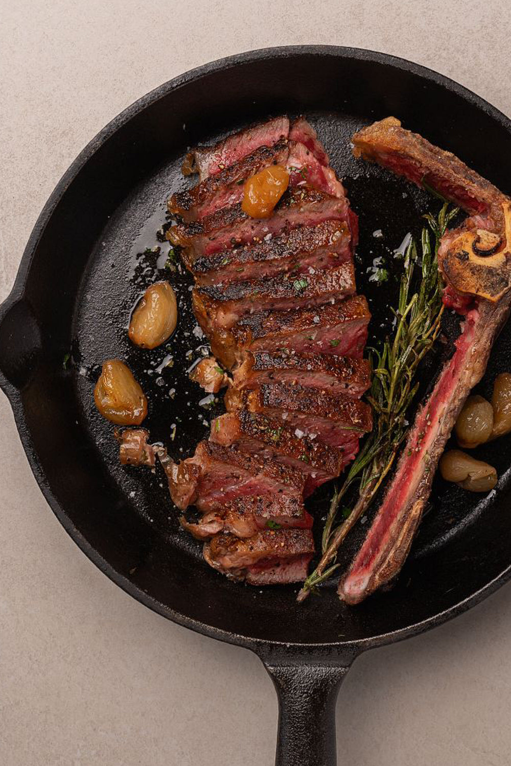 Seared NY strip steak in cast iron skillet with garlic, rosemary, and pearl onions, showing medium-rare interior.