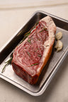 Raw NY strip steak seasoned with black pepper and rosemary, garnished with garlic cloves, in a metal tray.