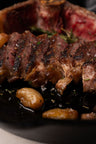 Sliced NY strip steak with seared crust, rosemary garnish, and roasted potatoes on dark plate.