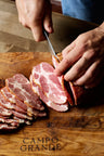Sliced cured pork meat with marbled pink and white sections being cut on a wooden board.