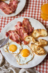 Sliced Ibérico coppa bacon, cooked crispy and arranged on a white plate with eggs and toast.