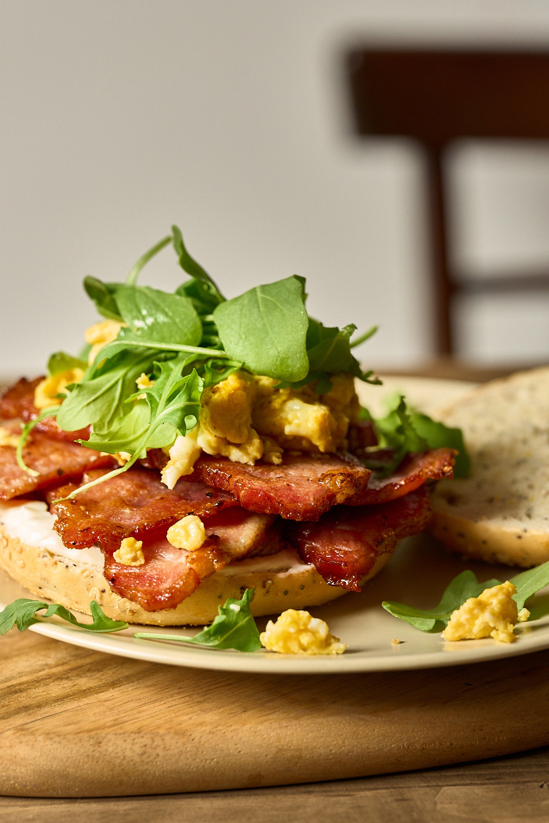 Sliced Ibérico coppa bacon layered on toasted bread with scrambled eggs, microgreens, and pea shoots on a white plate.