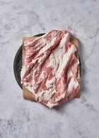 Raw pork belly steak with marbled red and white sections on kraft paper and dark plate.