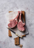 Three raw pork chops with marbled meat and fat on parchment paper and wooden cutting board with knife.
