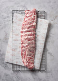 Raw ibérico pork loin with marbling and fat on black wire rack with printed paper wrapping.