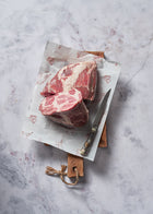 Raw Ibérico pork collar cuts displaying marbled meat and fat, placed on white paper atop wooden cutting board with knife.
