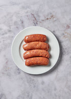 Four cooked chorizo sausages arranged on a white plate against a gray textured surface.