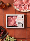 Packaged Ibérico boneless loin chops displayed on terracotta tiles with sliced meat on a white plate, wine glass, and cooking