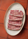 Four boneless pork loin chops with marbled meat surface arranged on a cream-colored oval plate.