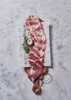 Raw flank steak with marbling on wooden board with rosemary sprigs and salt.