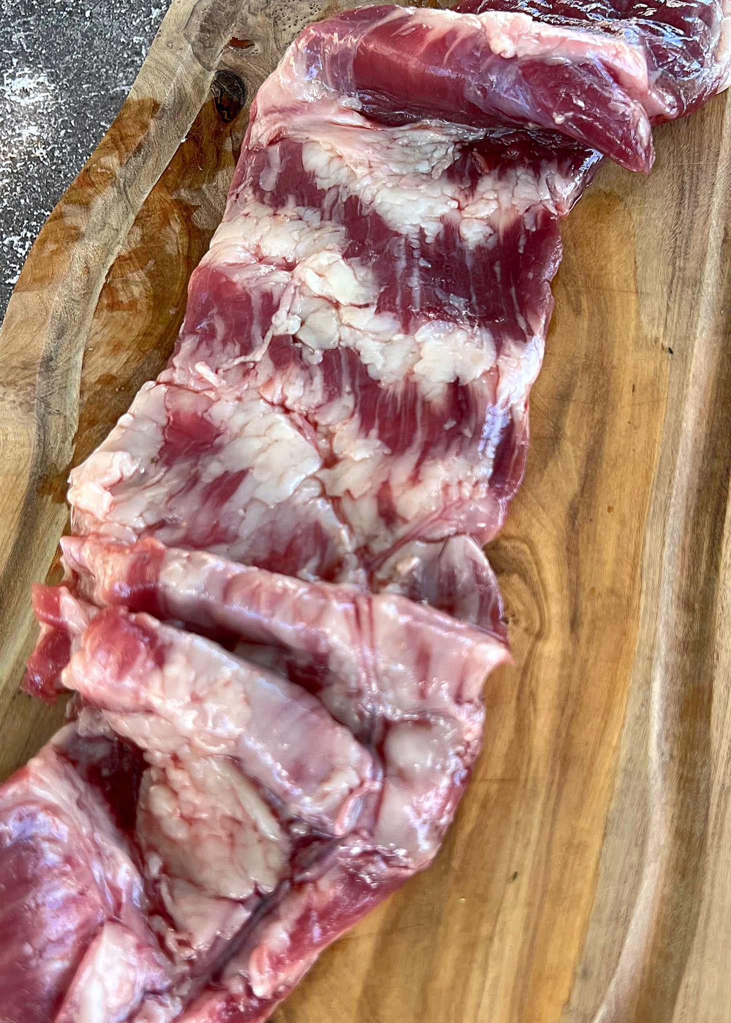 Raw Ibérico flank steak with visible marbling and fat on wooden cutting board.