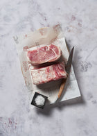 Two raw Ibérico loin roast cuts on parchment paper with a chef's knife and black dish of sea salt.