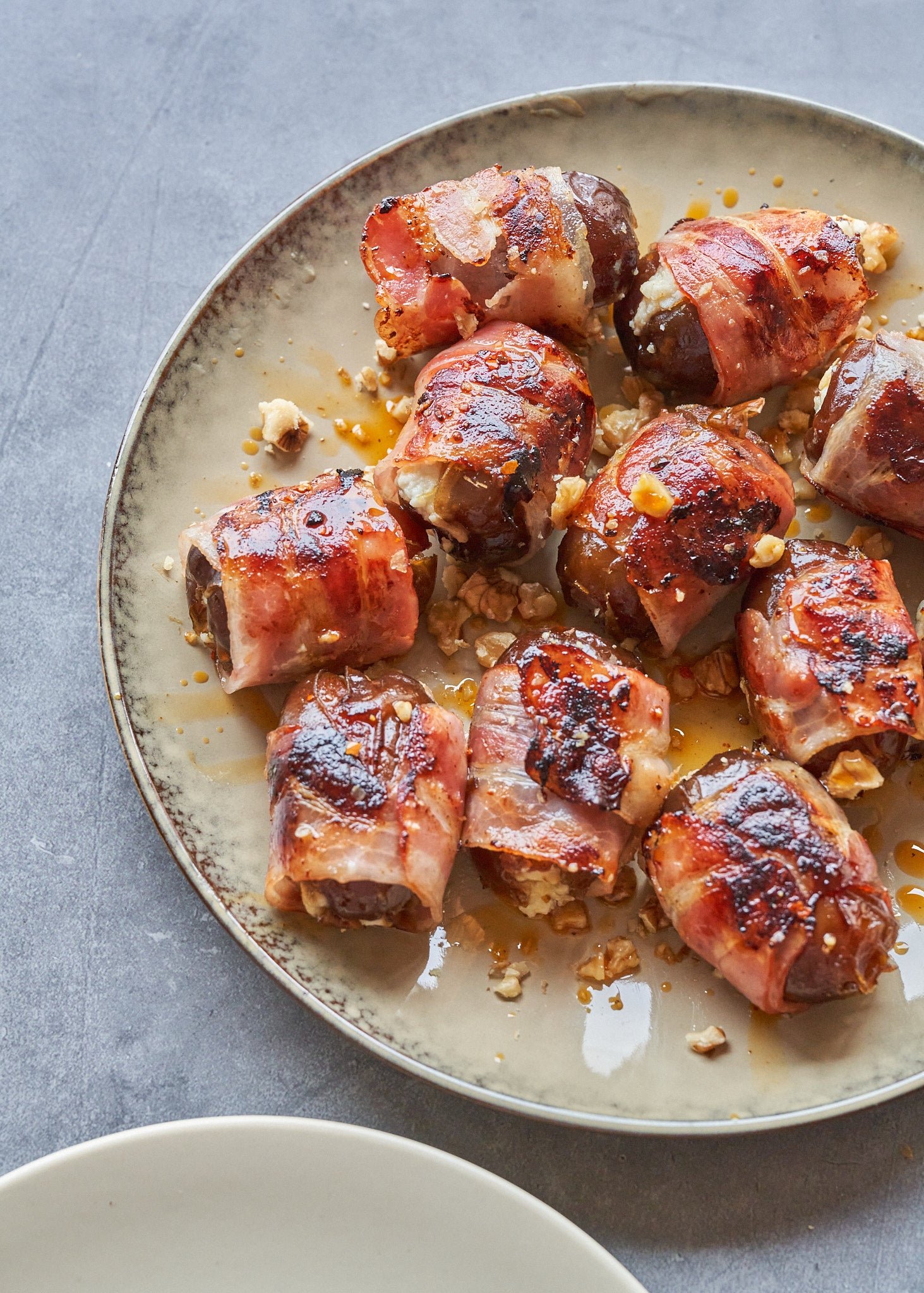 Cooked bacon pieces wrapped around filling, served on a beige ceramic plate with pan drippings.