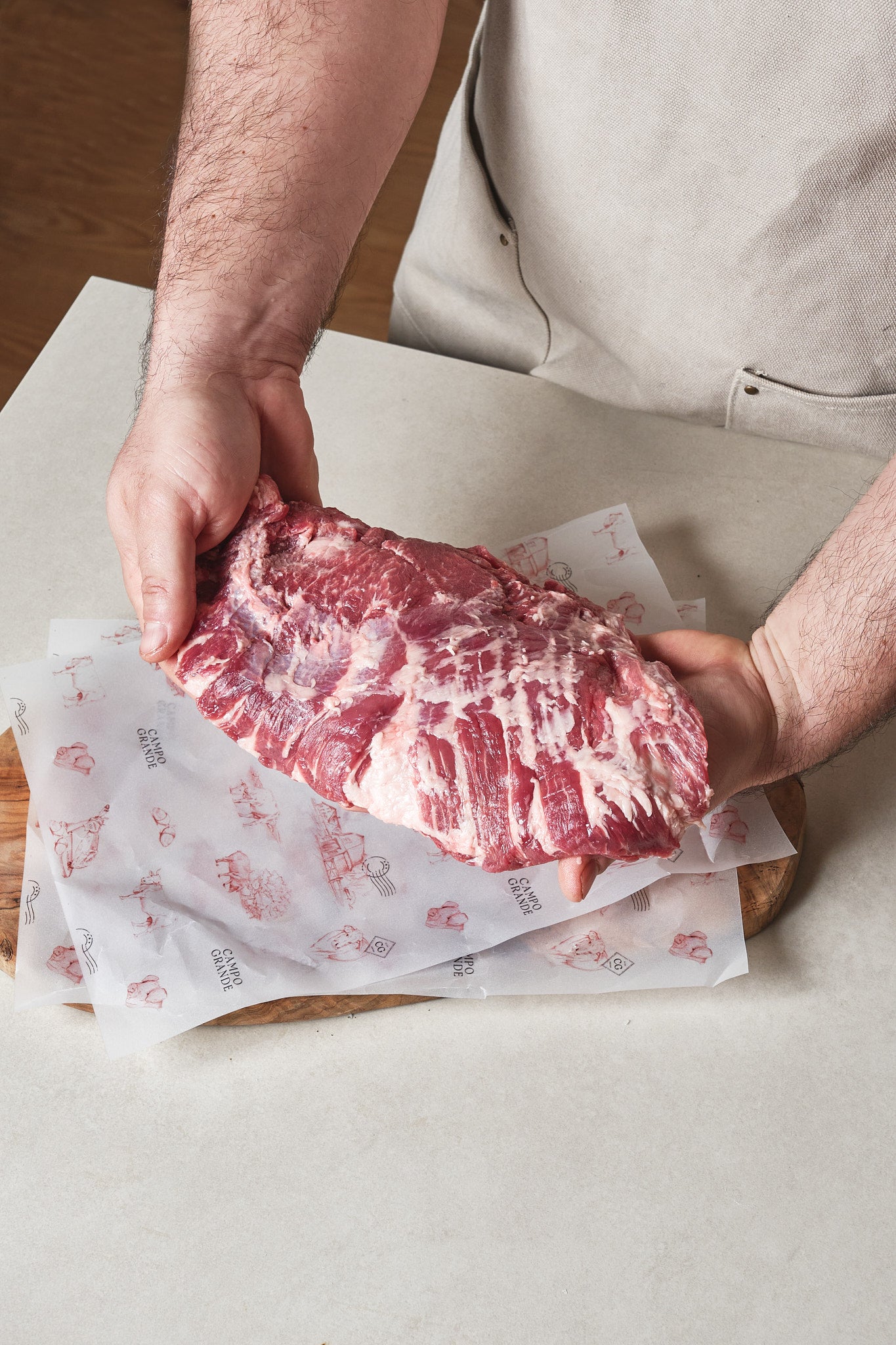 Raw Ibérico presa steak with marbled fat held in hands over butcher paper.