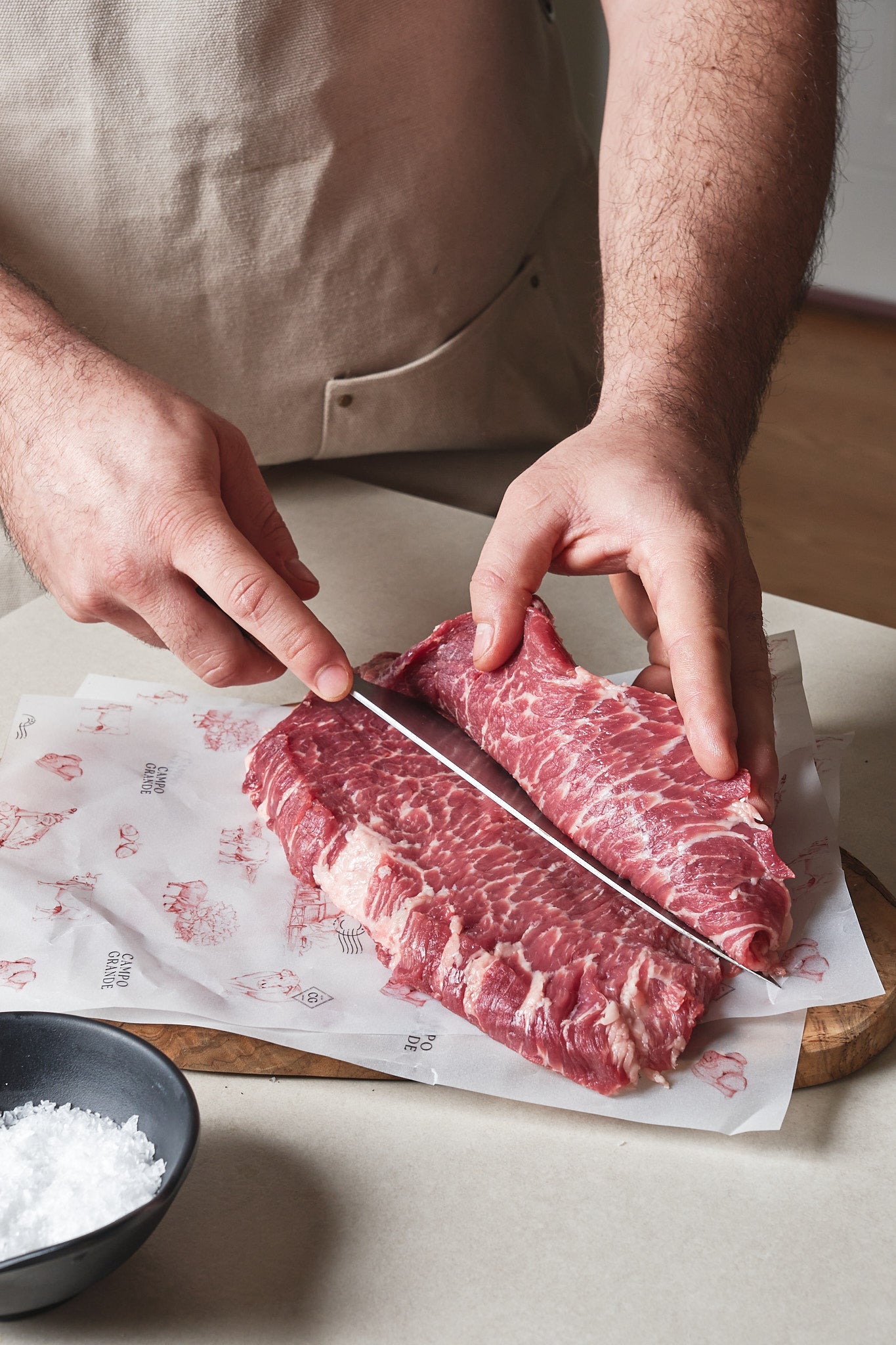 Raw ibérico presa steak with marbling being sliced by hands holding a knife on butcher paper.
