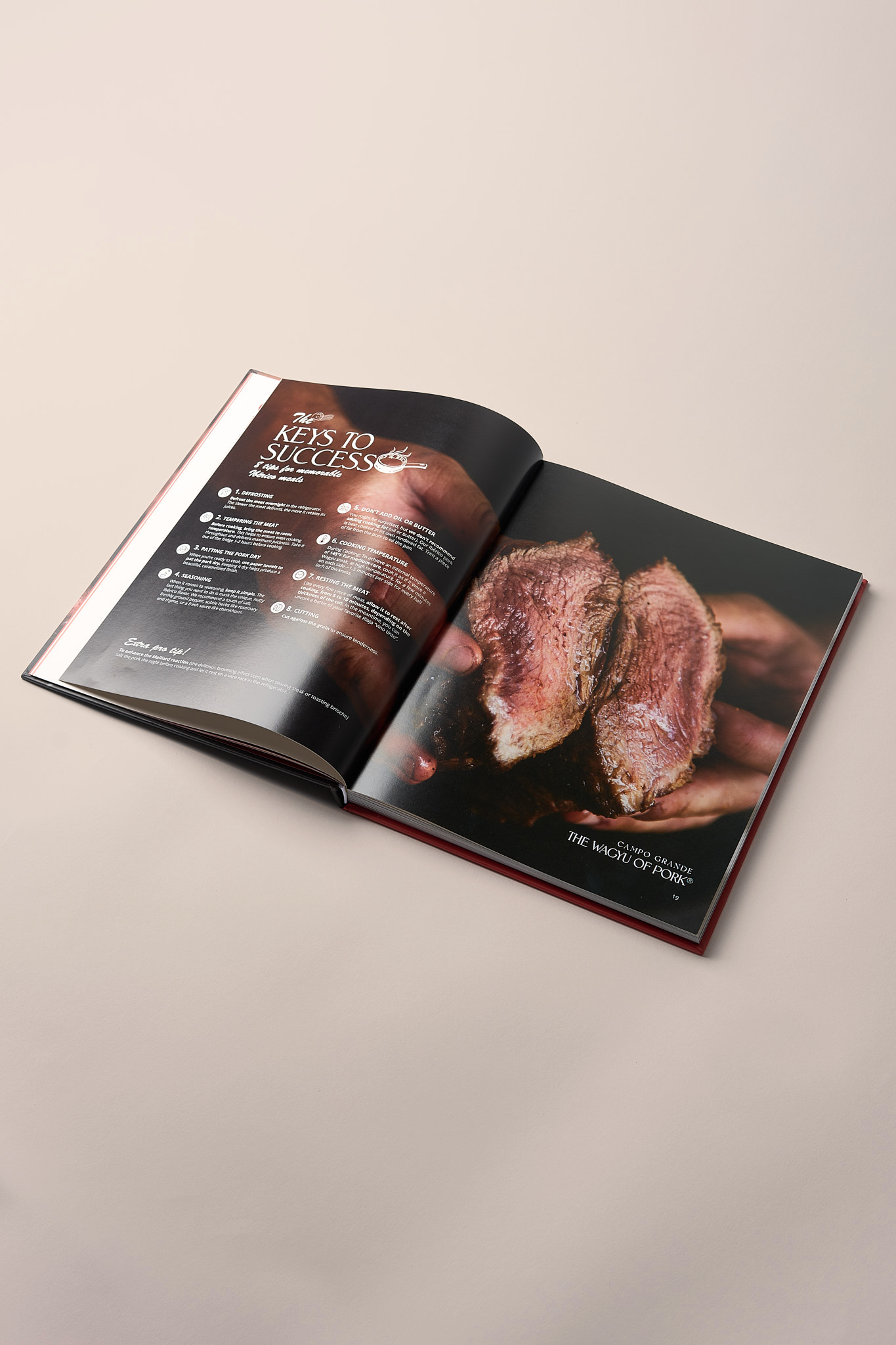 Hardcover cookbook opened showing "Keys to Success" chapter with cooked pork slices and instructional text on dark pages.