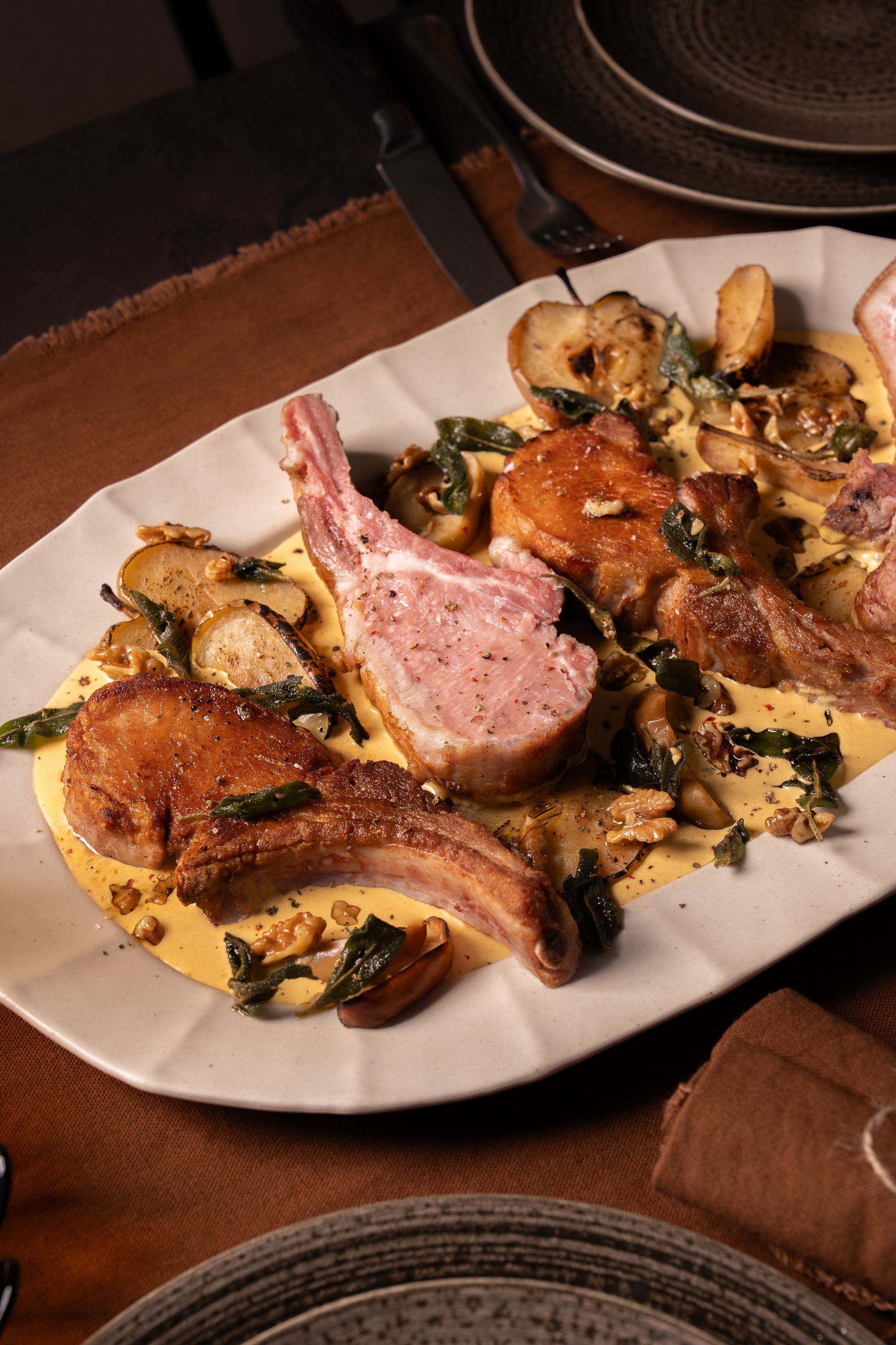 Four seared pork chops with visible bones served on white plate with sautéed mushrooms, greens, and sauce.