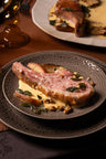 Seared pork chop with melted cheese and capers on a dark textured plate.