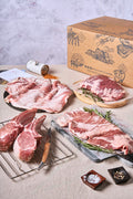 Assorted cuts of Ibérico pork on a table, including a rack of ribs, steak, and other meats, with a box labeled 'Campo Grande' in the background.