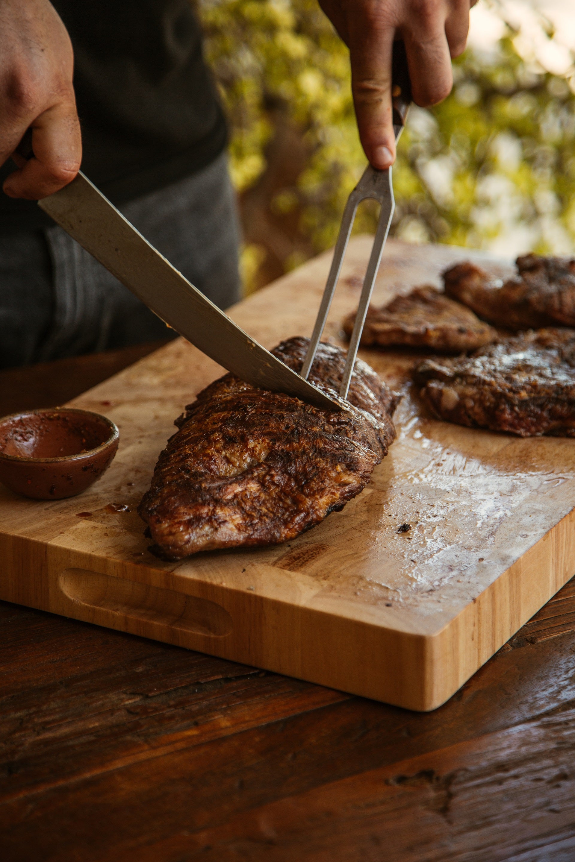 Seared Ibérico presa steak being sliced with knife and fork on wooden cutting board.