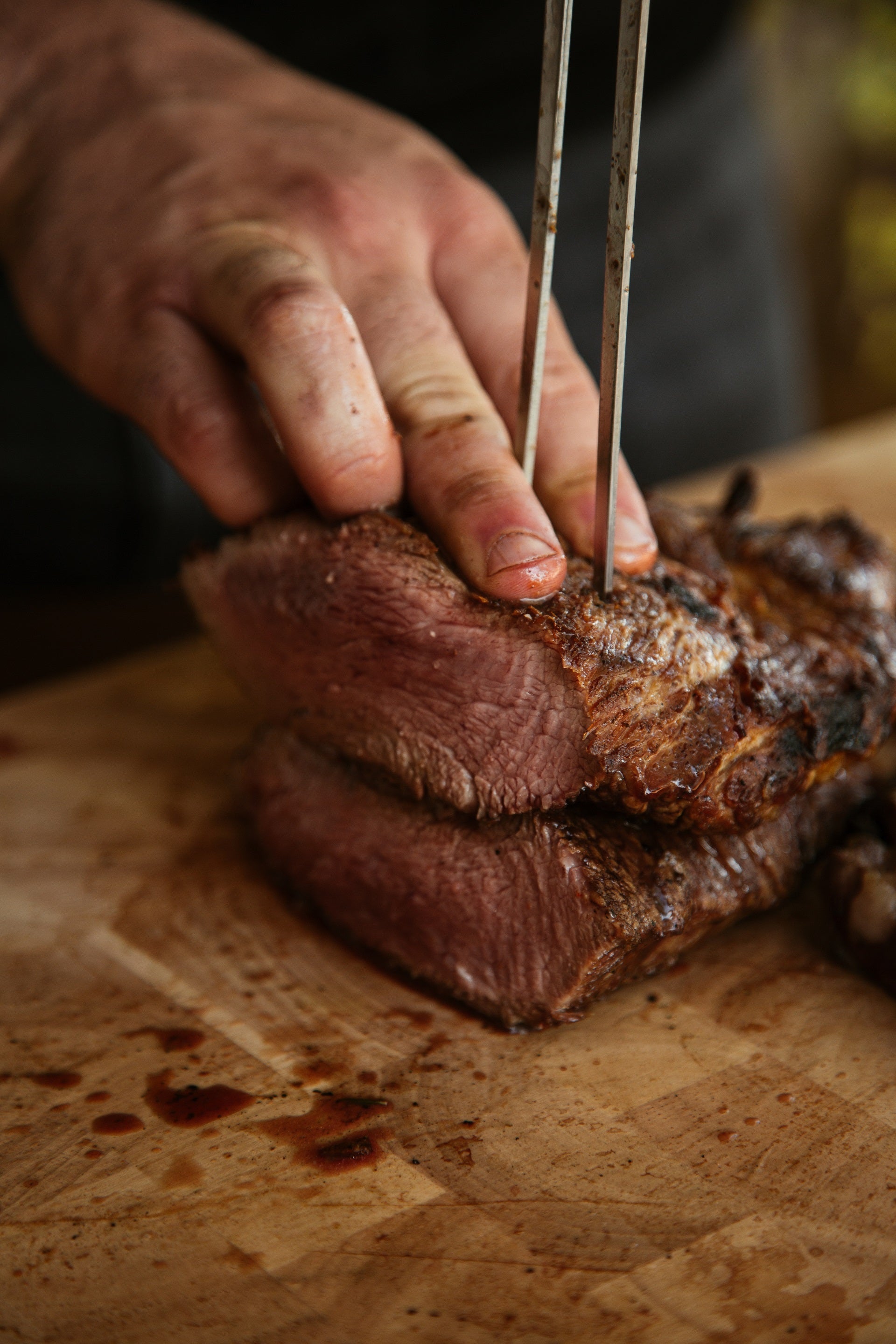 Raw Ibérico presa steak on wooden board being sliced with knife.