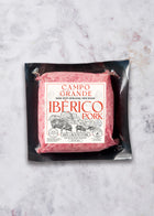 Ground Ibérico pork in sealed black vacuum package on marble surface.