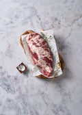 Raw Ibérico pork cut with marbled red and white meat on white paper with herbs and salt on wooden board.