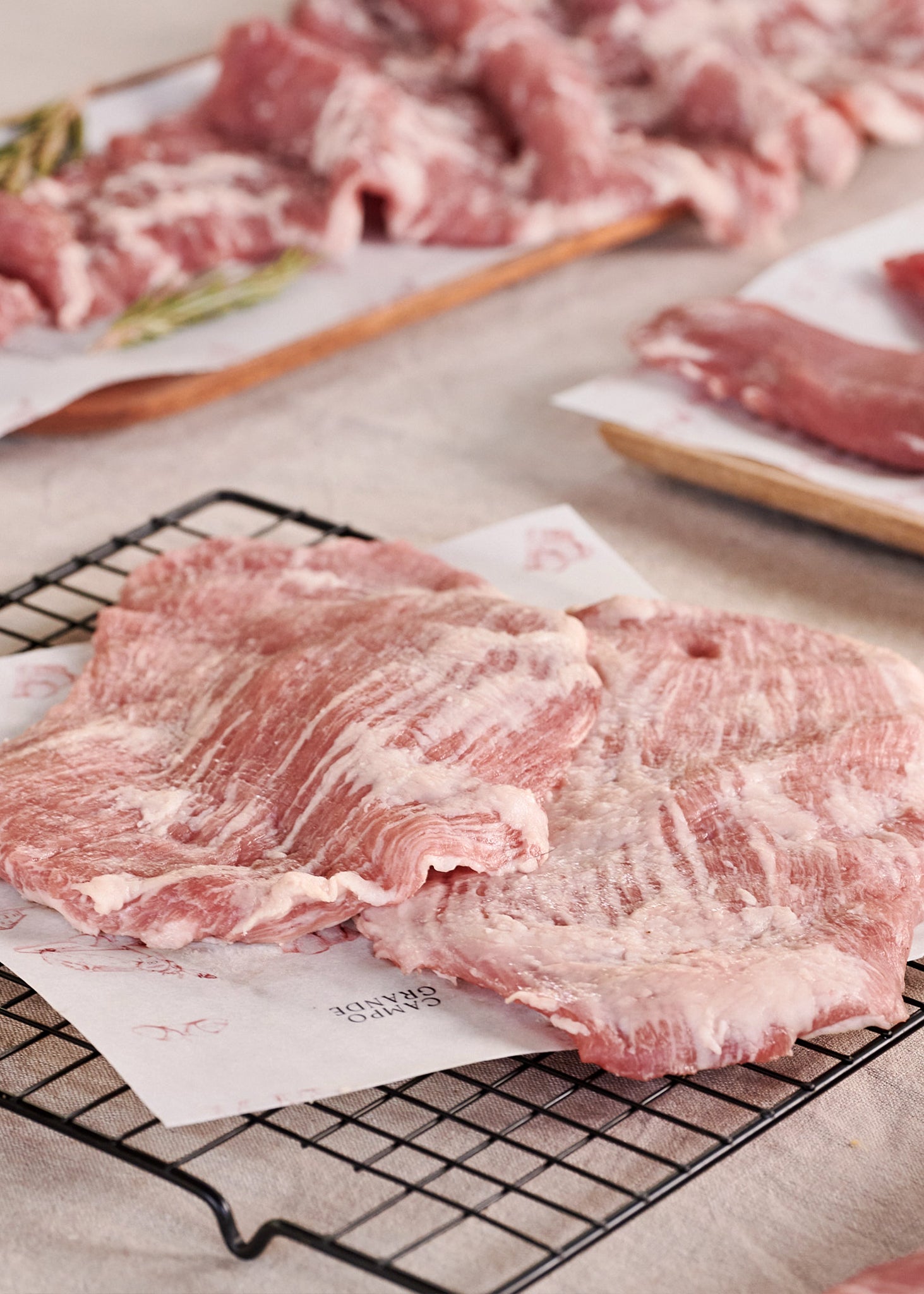 Sliced Ibérico jowl steak with marbling displayed on parchment paper and metal rack, with additional meat portions on wooden 