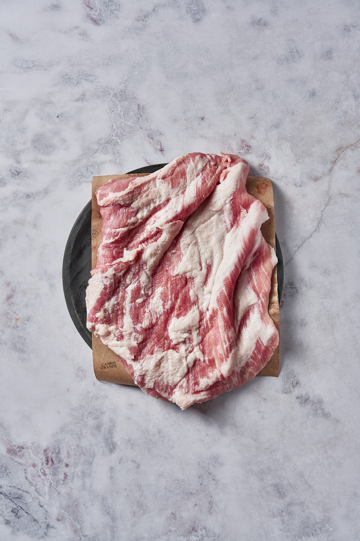 Sliced Ibérico pork with marbled red and white meat on wooden board with knife.