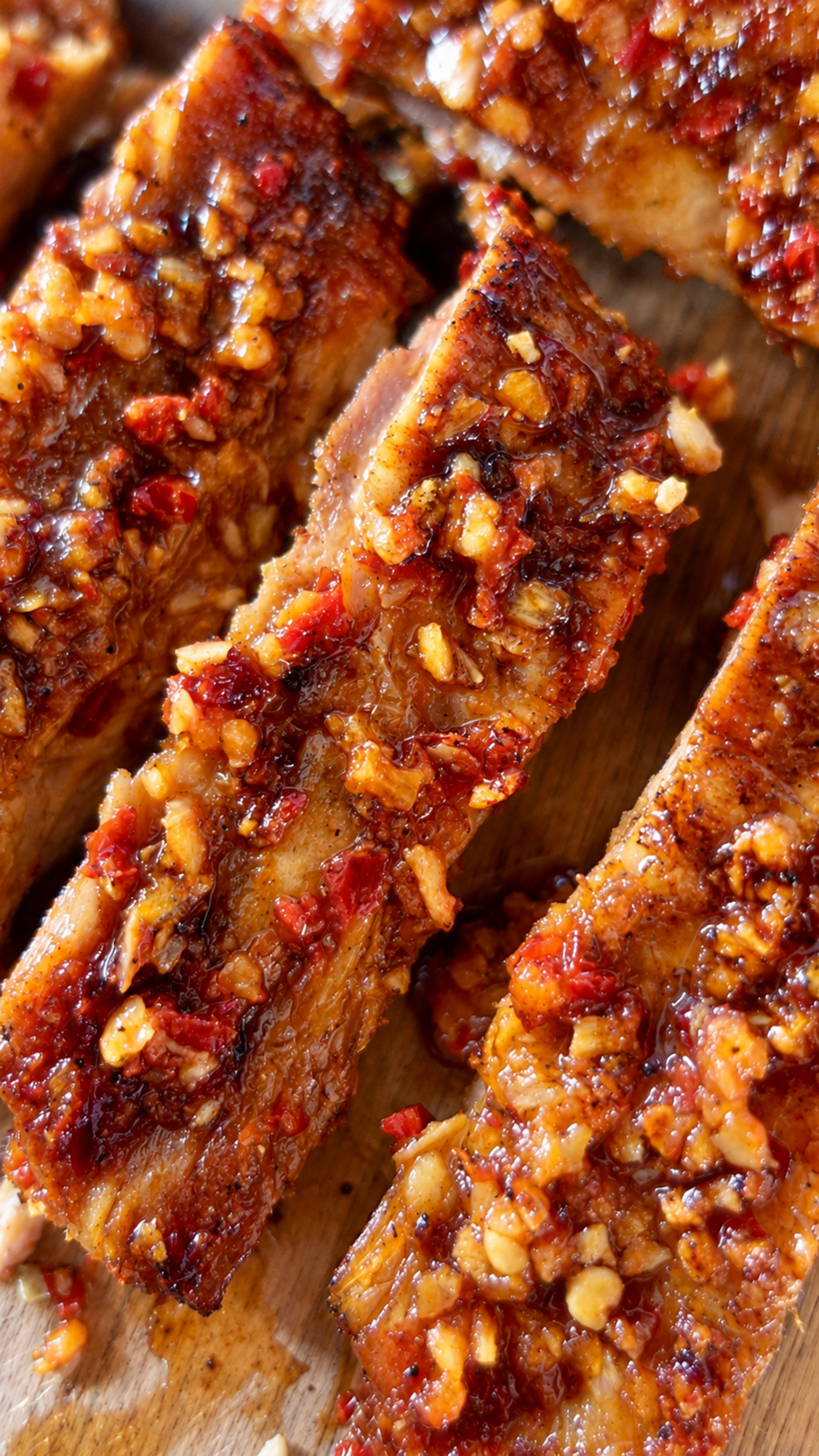 Cooked ribs with glossy caramelized coating and red pepper flakes on wooden surface.
