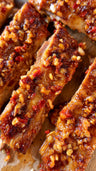 Cooked ribs with glossy caramelized coating and red pepper flakes on wooden surface.