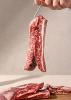 Hand holding raw wagyu outside skirt steak with marbled fat distribution above wooden surface.