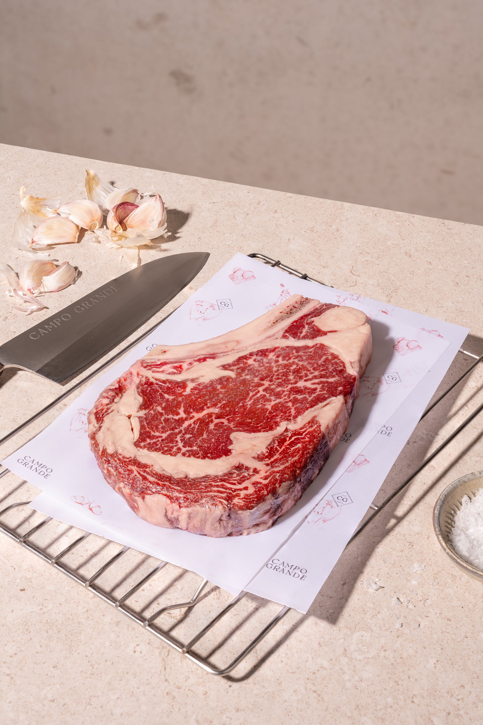 Raw wagyu beef steak with heavy marbling displayed on branded paper with knife and garlic cloves.