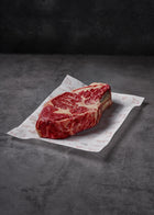 Bone-in beef steak with marbling on white butcher paper against dark gray surface.