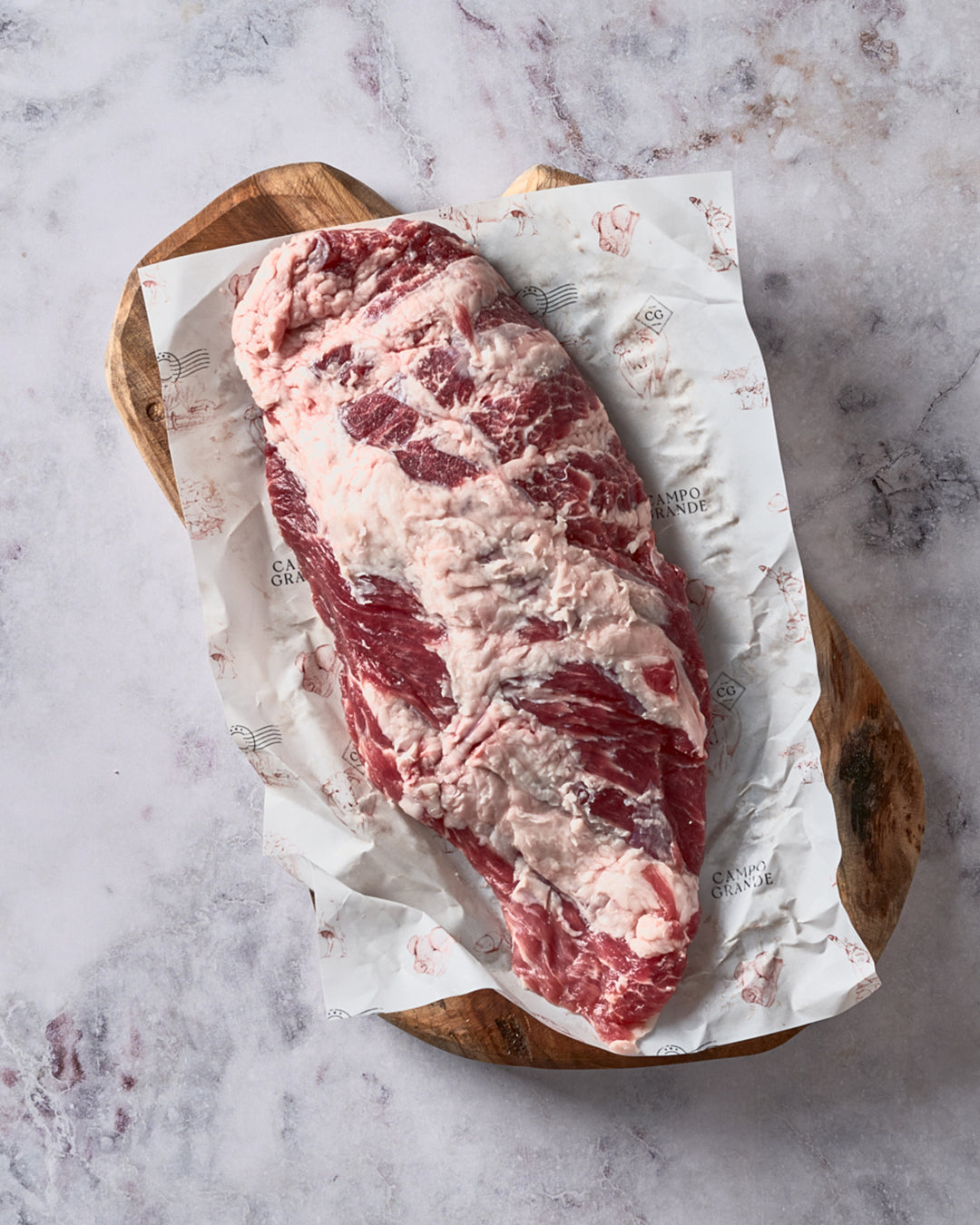 Raw Ibérico presa steak with marbling displayed on white butcher paper atop wooden board.