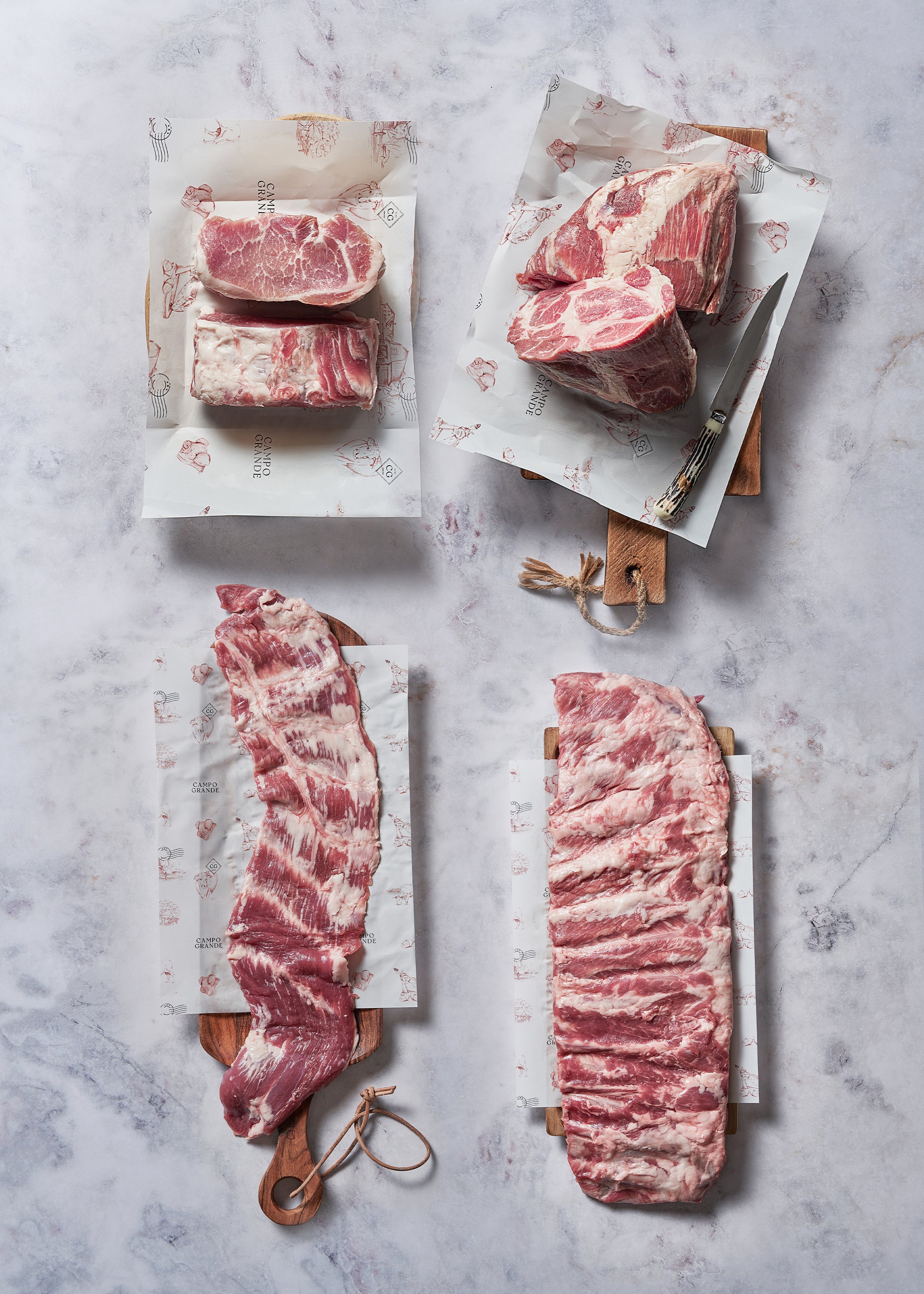 Four raw beef cuts displayed on white paper with wooden handles and a knife on marble surface.