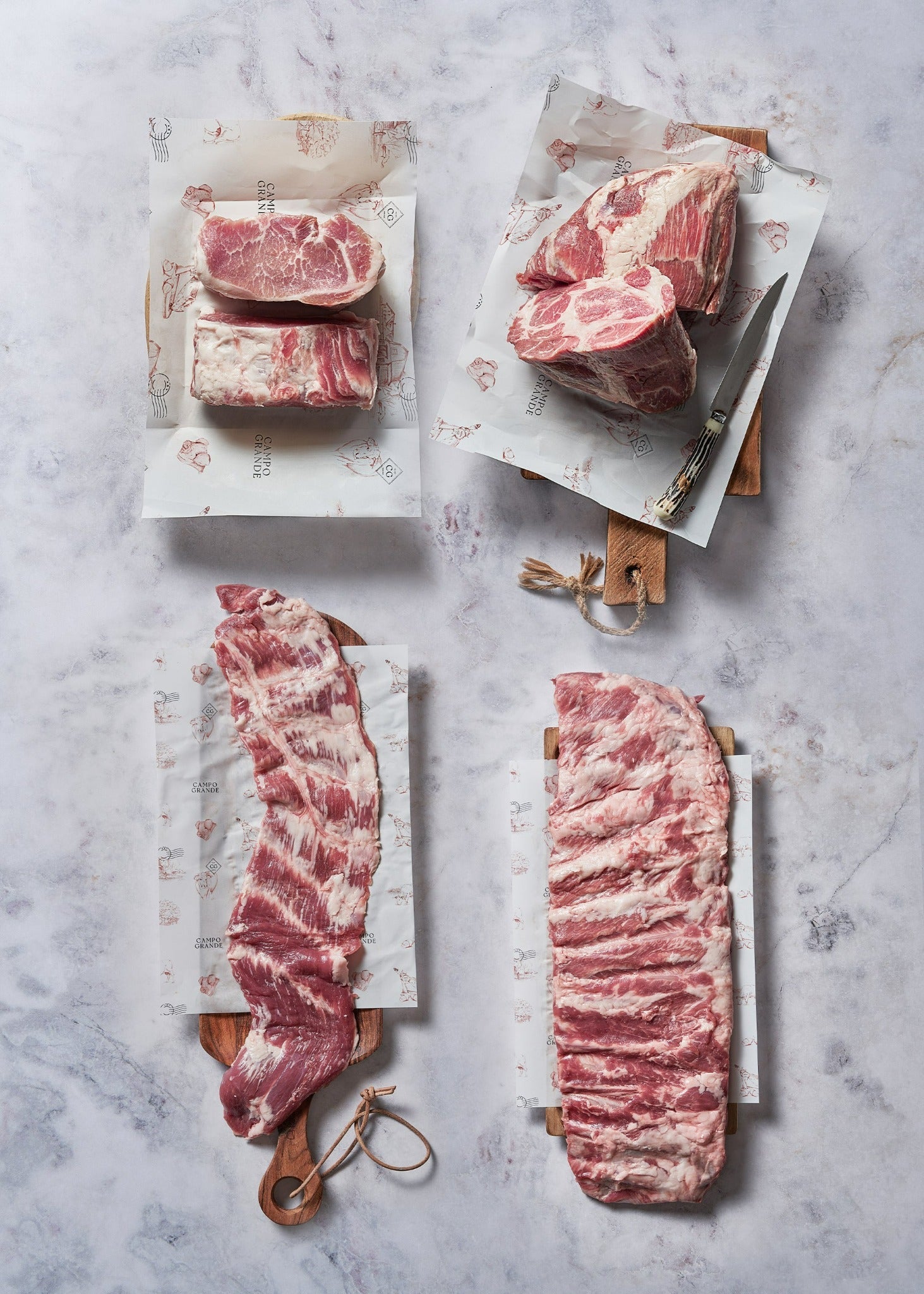 Raw beef steaks and cuts arranged on white butcher paper with wooden handles on marble surface.