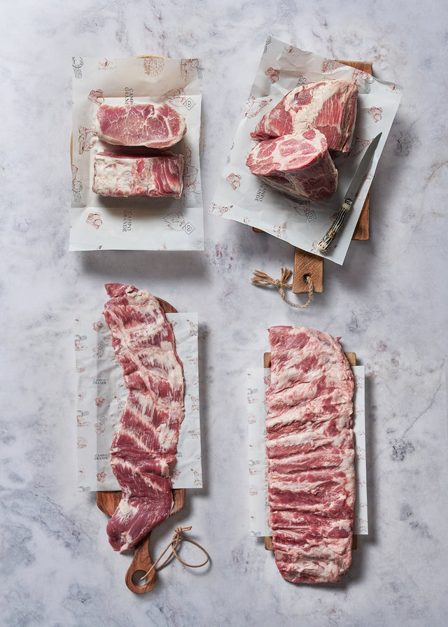 BBQ Grill Master Box (Free Shipping) image 1 of 7: Raw beef steaks and cuts arranged on white butcher paper with wooden handles on marble surface.