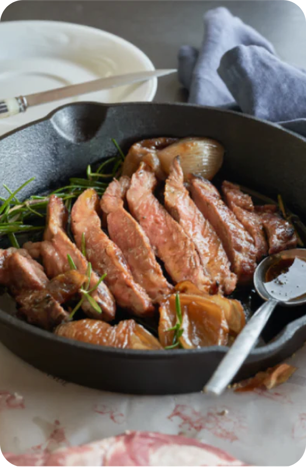 Sliced Ibérico pluma with roasted onions in a skillet