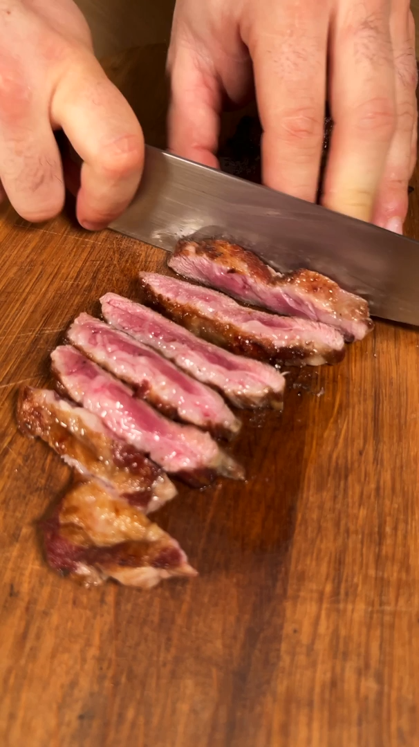 Cooked Ibérico pork being sliced on a wooden board